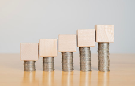 Empty wooden cube on top of stack of coins setting on wooden table. Calculate expense or cost...