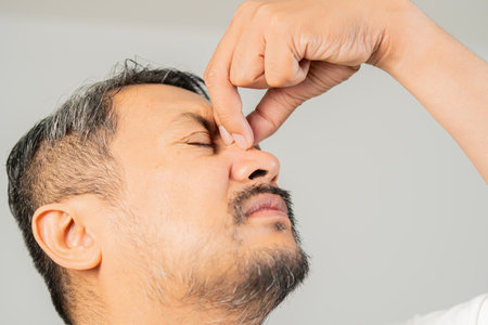 Close-up of adult man pinching the bridge of his nose, suffering from sinusitis or allergies and...