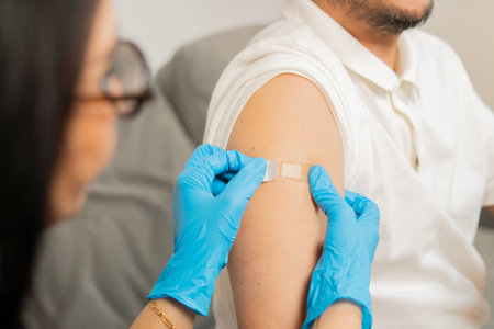 Doctor putting a bandage on the adult patient man after get a vaccinated against coronavirus at clinic. Back view, selective focus.の写真素材