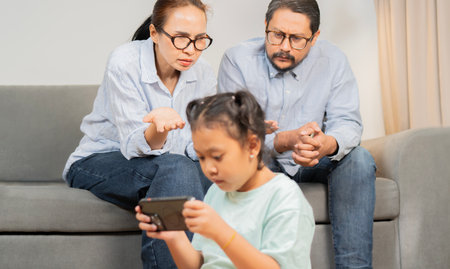 Smart phone addiction. Stressed parent talking about the issue of their daughter having a gaming addiction. Selective focus on parent.の写真素材