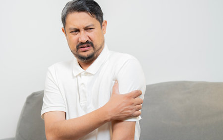 Man with pain in elbow. Pain relief concept. Middle age man feeling the pain in hand elbow at home. Male touching his painful elbowの写真素材
