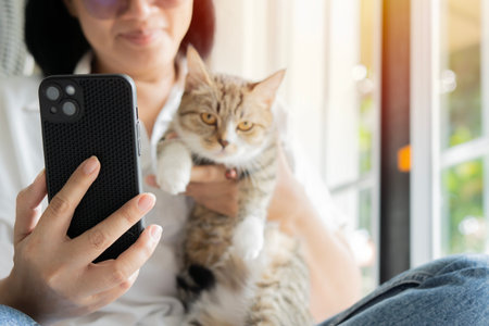 Happy woman taking selfie with cute cat while sitting on the floor near the door at home. Animal friendship concept.の写真素材