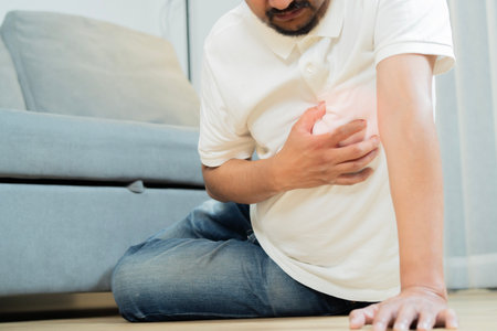 Cropped shot of Asian adult man sit on floor and holding his arms around his chest suffering from a heart attack. Heart problems concept.の写真素材