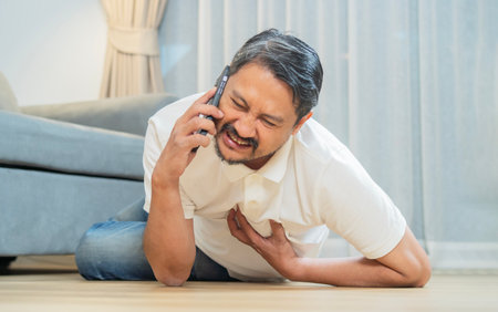 Mature man fell down on floor and calling emergency services, suffering from chest pain. Heart failure, first aid concept.の写真素材