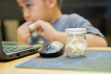 Stay at home, stay in school. Shot of an adorable little boy using a laptop while eating milk candy at home. Selective focus.の写真素材