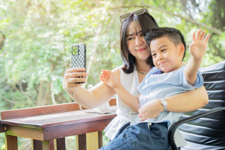 Mom and son in the park on a bench are photographed selfies on a mobile phone. Family photo session. Taking selfie.の写真素材