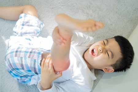 Little Asian boy lying on the carpet, hurting his knees and legs after falling on the floor. Selective focus.の写真素材