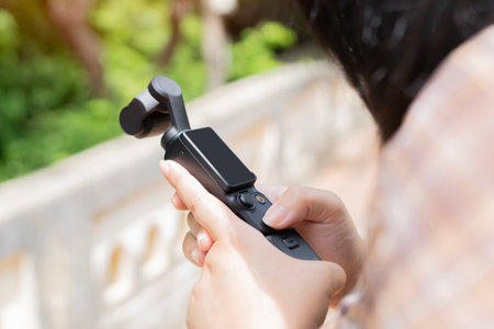 Young woman holding a tiny modern video camera and set up her device to take photos and videos while...