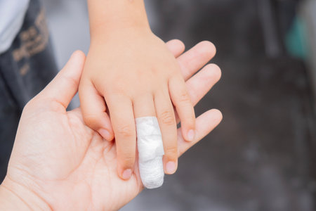 Large hand of mother and small hand of little son with bandaged finger. Injured finger of a child wrapped in a white bandage, closeupの写真素材