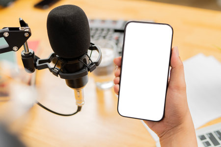 High angel view of a podcaster behind microphone holding a smartphone with isolate screen. Copy space.の写真素材