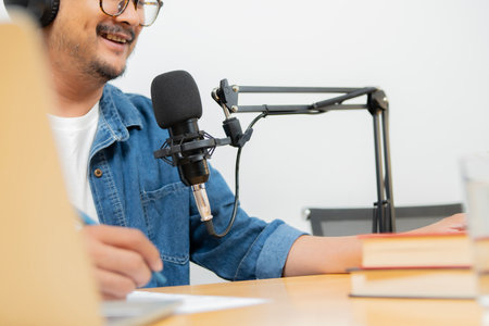 Man podcaster influencer blogger smiling while broadcasting his live audio podcast in studio using headphones, laptop. Male radio host making podcast or interviewの写真素材