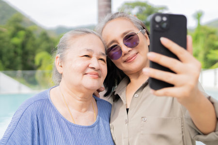 An attractive middle-aged woman with her adult daughter doing selfie nearby a swimming pool, vacation and travel.の写真素材