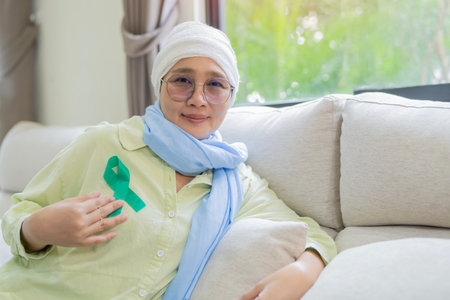 Face, elderly woman or cancer patient with green ribbon sitting on sofa at home. Healthcare,...