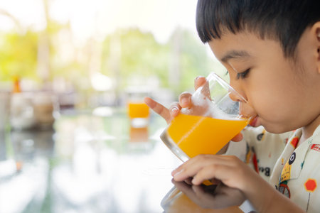 Side view of Asian boy drinking fresh orange juice during breakfast at outdoor with copy space. Close-up, selective focus.の写真素材