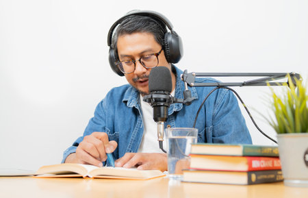 Podcasters with eyeglasses and headphone reading a book while recording audio content at home studio. Selective focus.の写真素材