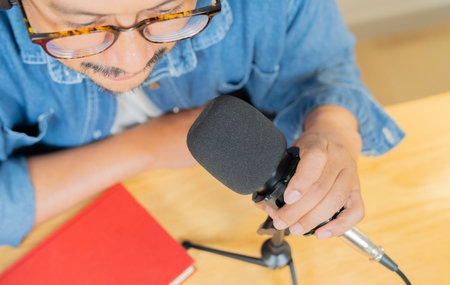 High angle view of bearded man with red book holding microphone doing podcast session while sitting at home.の写真素材