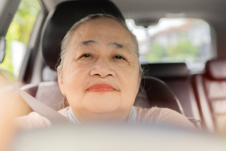 Happy senior Asian woman driving car alone, enjoying car ride. Safe driving for elderly adults, older driver safety. Portrait senior image.の写真素材