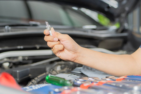 Hand of the auto mechanic holding the old spark plug on blurred engine car on background. Car...