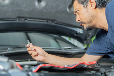 Side view of Asian handsome man with beard changes spark plugs in his car. Replacing spark plugs in the car.の写真素材