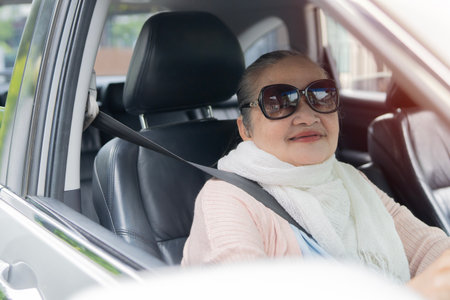 Portrait of a happy senior woman in sunglasses driver looking out the car window. Concept of an active people during retirement ageの写真素材