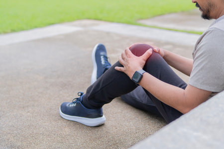 Rear view mature man suffering from painful knee while sitting on floor at outdoor with copy space. Healthcare, medicine and people concept.の写真素材
