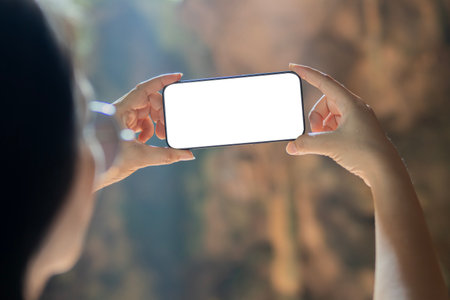 Person holding blank screen smartphone on tropical vacation. Time off on holidays. Hand holding blank mock up phone screen on tropical cave hall.の写真素材