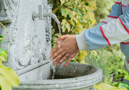 Hands catching water from an old faucet style in the garden. Hands turning on a tap outdoors, water flowing.の写真素材