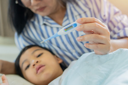 Sick thermometer, child health and mother reading fever, care for boy with virus in bed of house. Kid resting with flu while mom takes temperature in bedroom of home with loveの写真素材