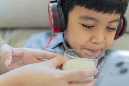 An unhappy child refuses to drink milk, he pressed his lips together in frustration while using his phone. Close-up, selective focus.の写真素材