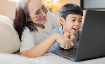 Happy mother and her little son using laptop computer at home, Smiling Asian mom showing cartoons to...