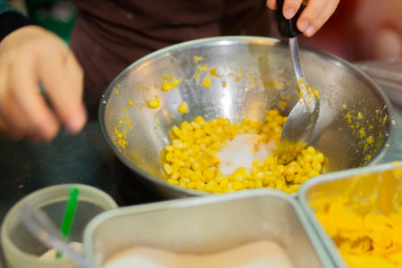 Close up hand of street vendor during cooking for mixed corn butter, sweet and simply Thai dessert. Selective focus.の写真素材