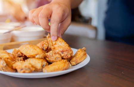 People hands taking the fried chicken wings in a white plate on a wooden table with copy space. Selective focus.の写真素材