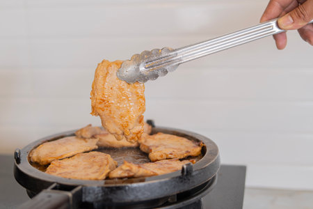 Cook pork slices in a hot pan by using tong, Slices of pork frying in a pan.の写真素材