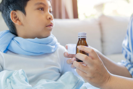 Cough syrup in bottle. Cute toddler boy with mom holding in hands natural syrup. Health medicine concept. Pediatrician prescription for a child.の写真素材