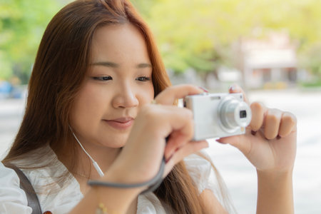 Happy Asian girl standing and taking pictures with digital camera at park. Girl with mini digital...