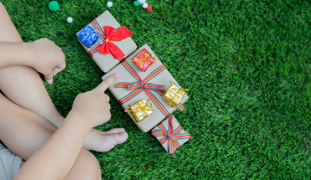 Top view of boy sitting on the grass in decorated area on Christmas Eve in festive mood and counting xmas gifts. Copy space. Christmas season concept.の写真素材