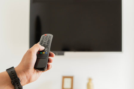 A man hand holding a remote control in front of a smart TV indoors. Banner with copy space. Watching TV Concept.の写真素材