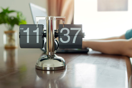 Vintage flip clock on table in office with blurred background of woman work with laptop. Time...