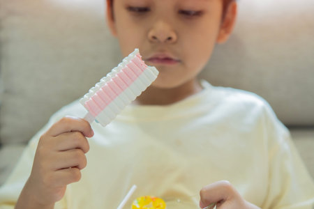 Cute little Asian child sitting at the livingroom and eating marshmallows. Selective focus.