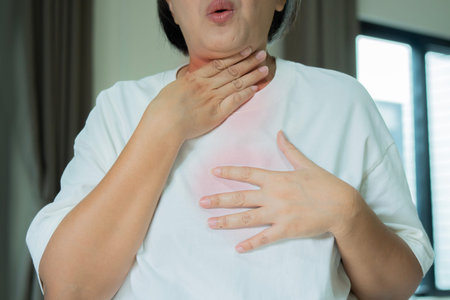 Woman suffering from Acid Reflux Or Heartburn standing in livingroom at home. Mature woman suffering...