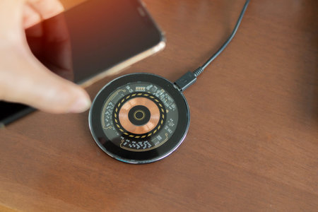Hand placing a modern smartphone onto a circuit board design wireless charging pad on a wooden desk....