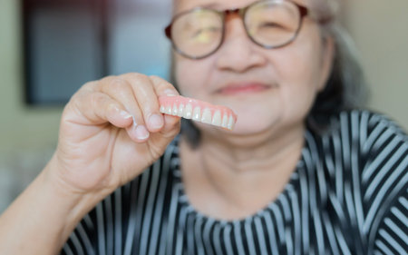 Happy senior lady holds and shows her new dental implant and jawline with a pair of teeth. Concepts...