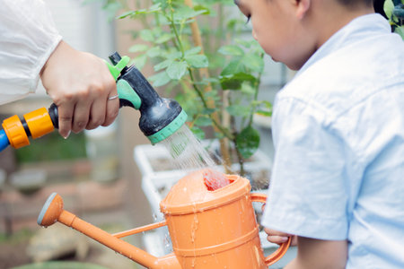 Happy farmer family take care of plant together in the garden. Mother and son watering plant together. Child education of nature and plant growing learn activity concept.