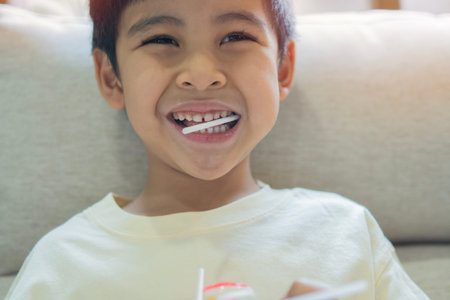 Portrait of young happy and excited male kid smiling cheerful eating a lollipop sitting on sofa at...