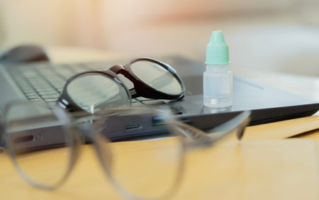 Eye drops and glasses on laptop at workplace. Treatment and prevention of eye diseases. Selective...