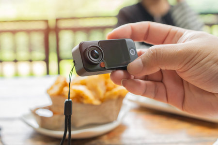 Cropped view close-up of unrecognizable photographer holding mini black action camera while taking...