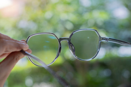 Woman holding the eye glasses spectacles with shiny grey frame on green nature background. Close-up,...