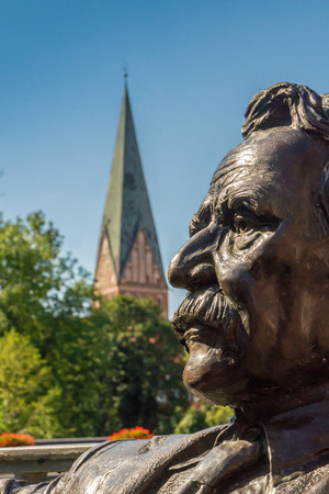 View of a sculpture of Mark Twain at a public place. Background the Nicolai Church. One of the most visit places at Luenburg Germanyのeditorial素材