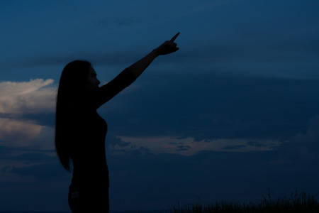 Woman pointing to the sky in the evening light in the shadows.の写真素材