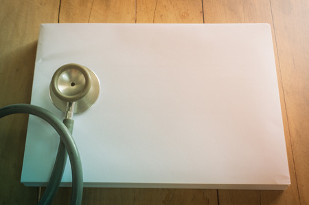 Doctors Stethoscope on a blank paper with wooden plate for medical concept in vintage styleの写真素材